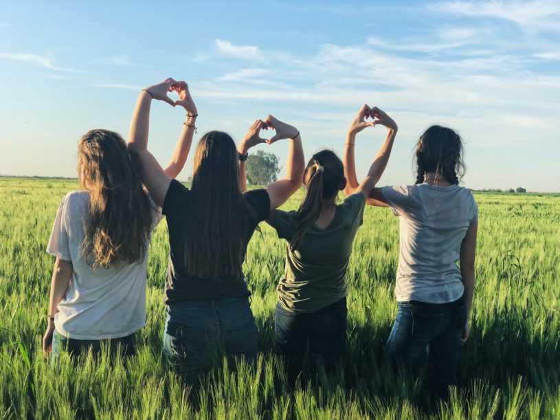 Women in a field making heart symbols with hands